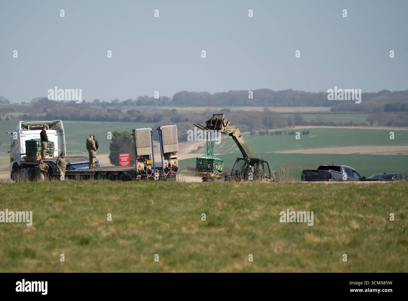 Camion logistico a pianale MAN SX 6x6 dell'esercito britannico con gru in un campo di erba verde, che recupera i pallet CDS da una caduta di paracadute Foto Stock