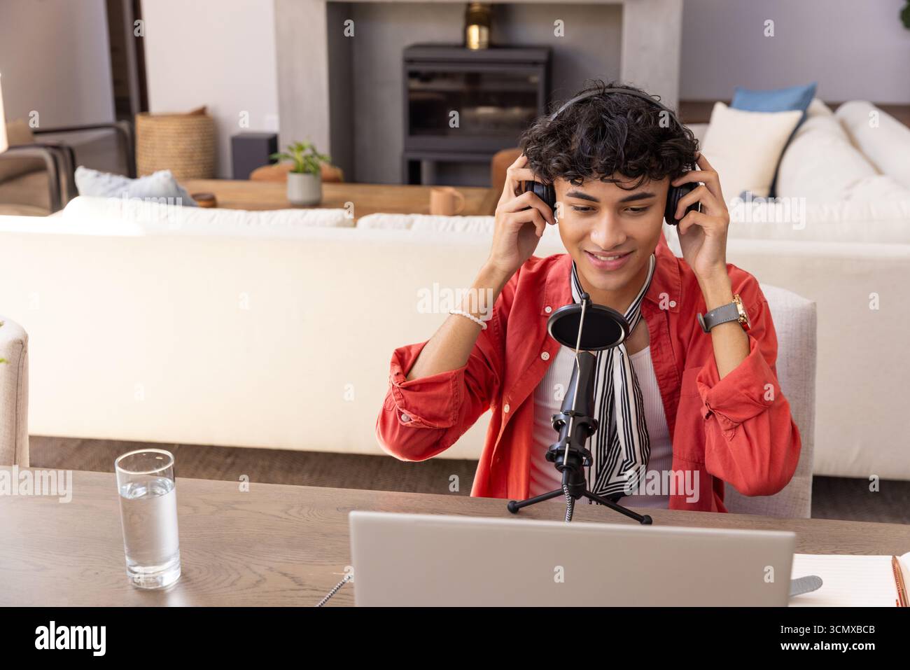 Uomo che parla al microfono indossando le cuffie, che utilizza il computer portatile al tavolo in salotto Foto Stock