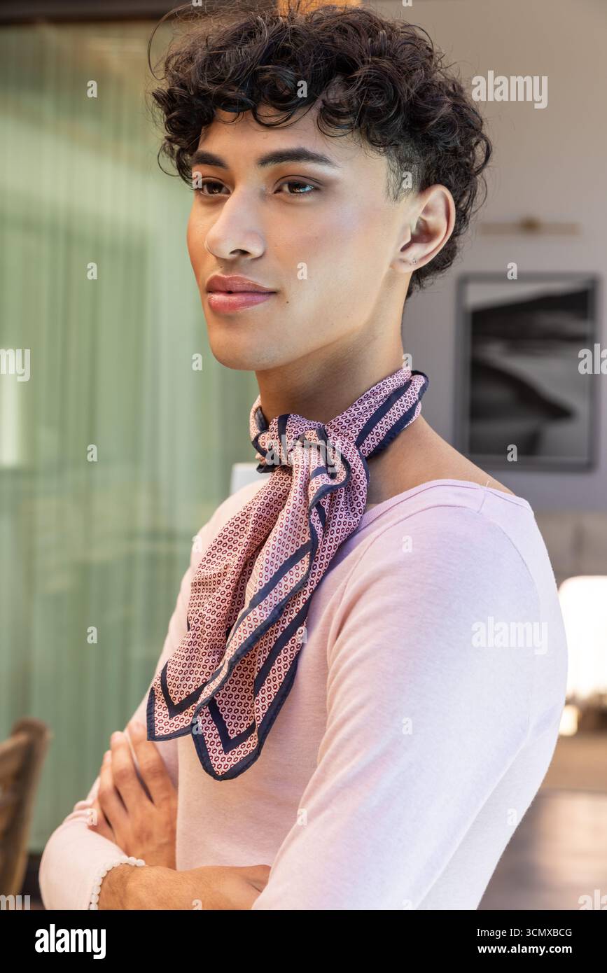 Uomo asiatico in piedi braccia incrociate nel soggiorno con top rosa e foulard di seta a motivi geometrici Foto Stock