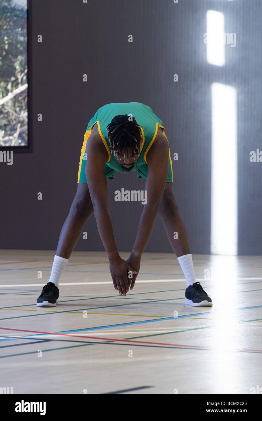 Uomo afroamericano che si allunga in campo con uniforme sportiva con marcature da basket Foto Stock