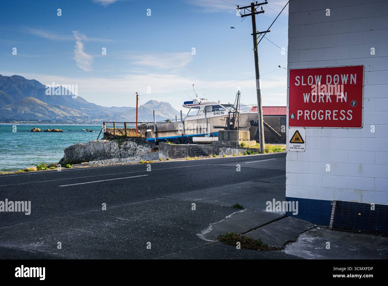 Strada costiera accanto al mare blu con vista sulle montagne e cartello dei lavori in corso presso la penisola di Kaikura, South Island, nuova Zelanda Foto Stock