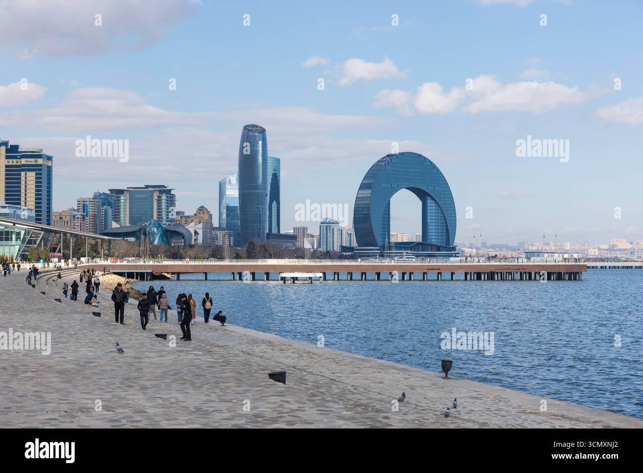 Baku, Azerbaigian - 23 marzo 2025: Scena urbana sul lungomare che mostra l'architettura moderna, una passerella pedonale e la gente che gode di una vista panoramica della città u Foto Stock Baku, Azerbaigian - 23 marzo 2025: Scena urbana sul lungomare che mostra l'architettura moderna, una passerella pedonale e la gente che gode di una vista panoramica della città u Foto Stock
