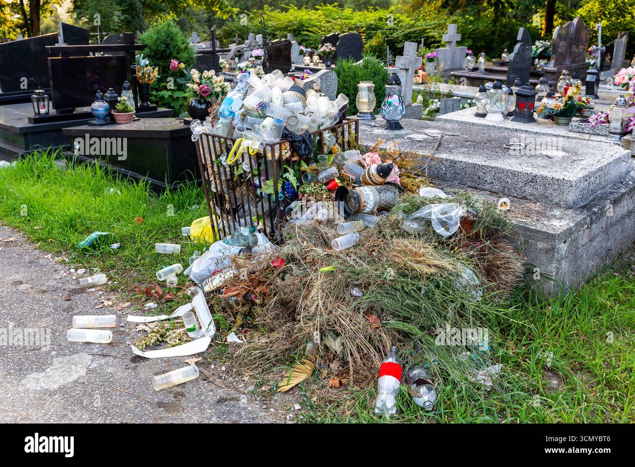 Contenitore dei rifiuti traboccante di lampade usate, candele, fiori e ghirlande artificiali e altre tombe decorate nel cimitero in Polonia, plastica Foto Stock