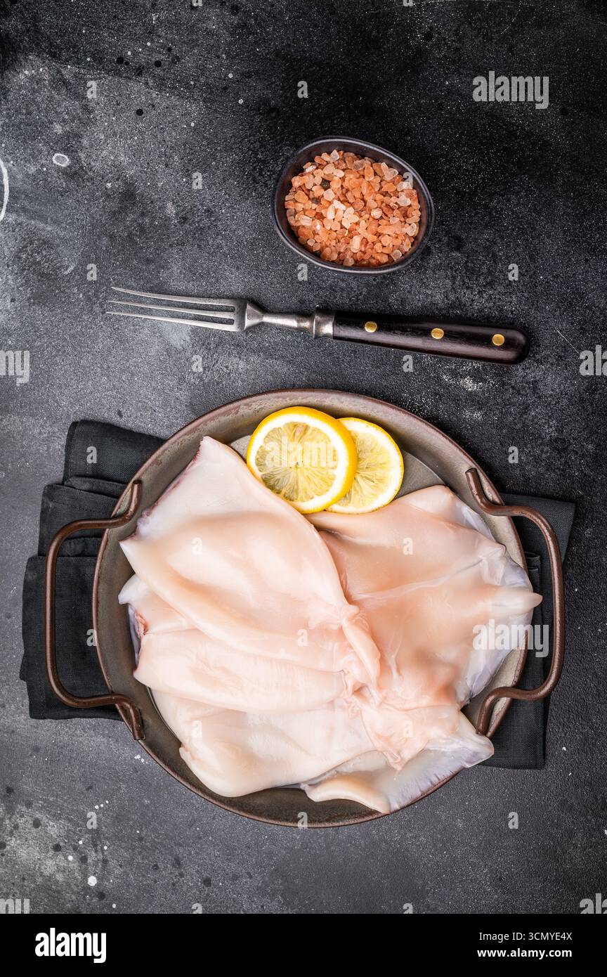 Calamari crudi freschi pronti per la preparazione, perfetti per sushi, patatine fritte o piatti gourmet a base di pesce. sfondo nero. vista dall'alto. Foto Stock