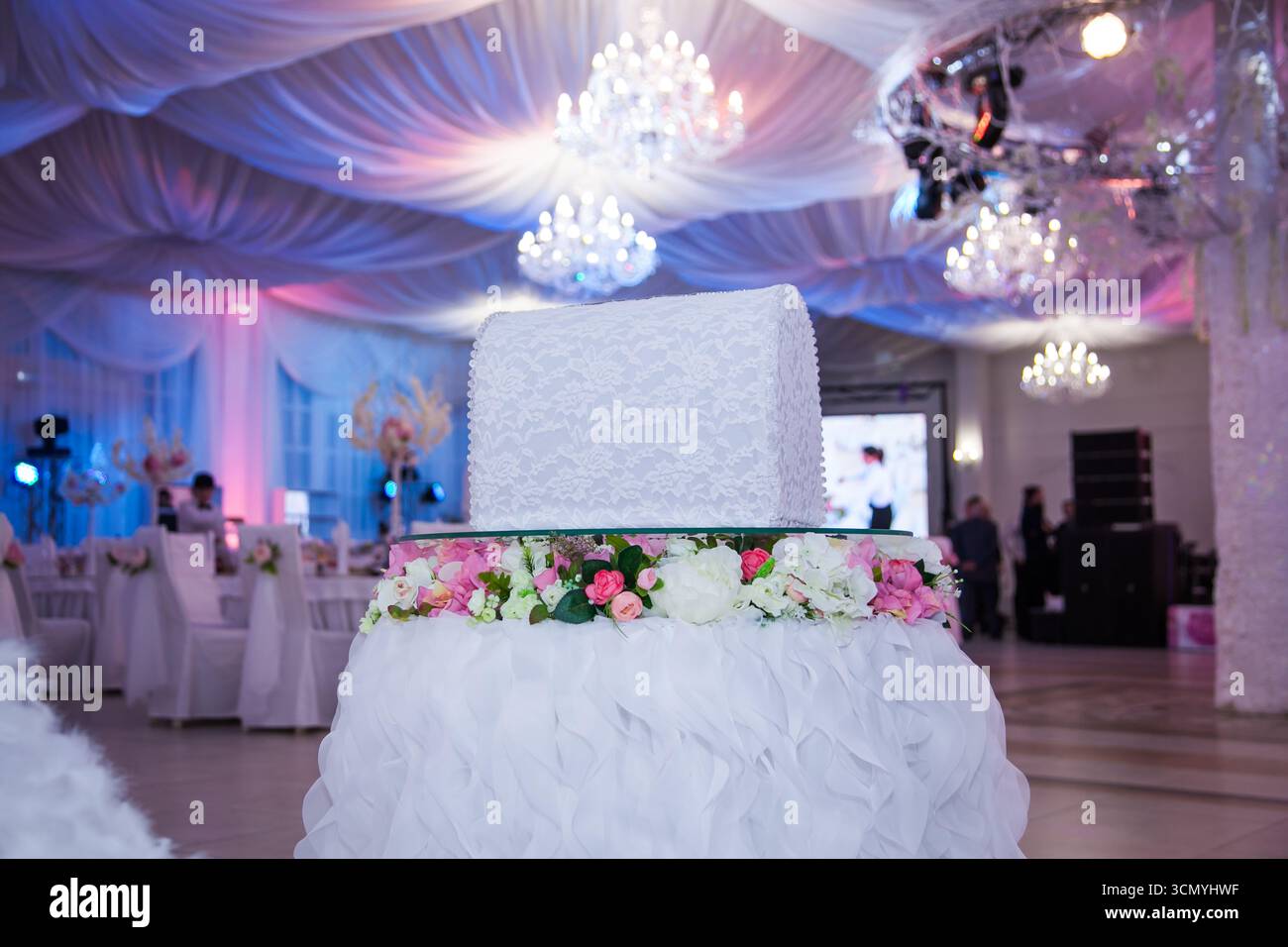 Un portamonete splendidamente organizzato si trova in cima a un piedistallo decorato con fiori, circondato da un raffinato decor per ricevimenti. Un'illuminazione soffusa esalta l'atmosfera romantica Foto Stock