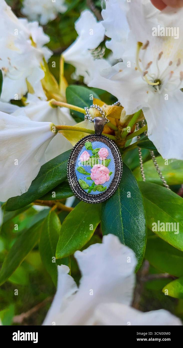 Ciondolo con ricamo a nastro realizzato a mano e motivo floreale su sfondo di alberi in fiore Foto Stock