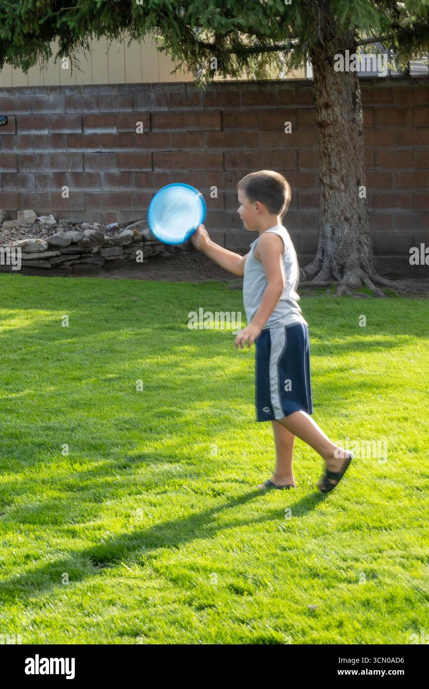Un bambino di sette anni gioca con un disco volante nel suo cortile in un pomeriggio estivo di sole, 2025, Great Falls, Montana, Stati Uniti Foto Stock