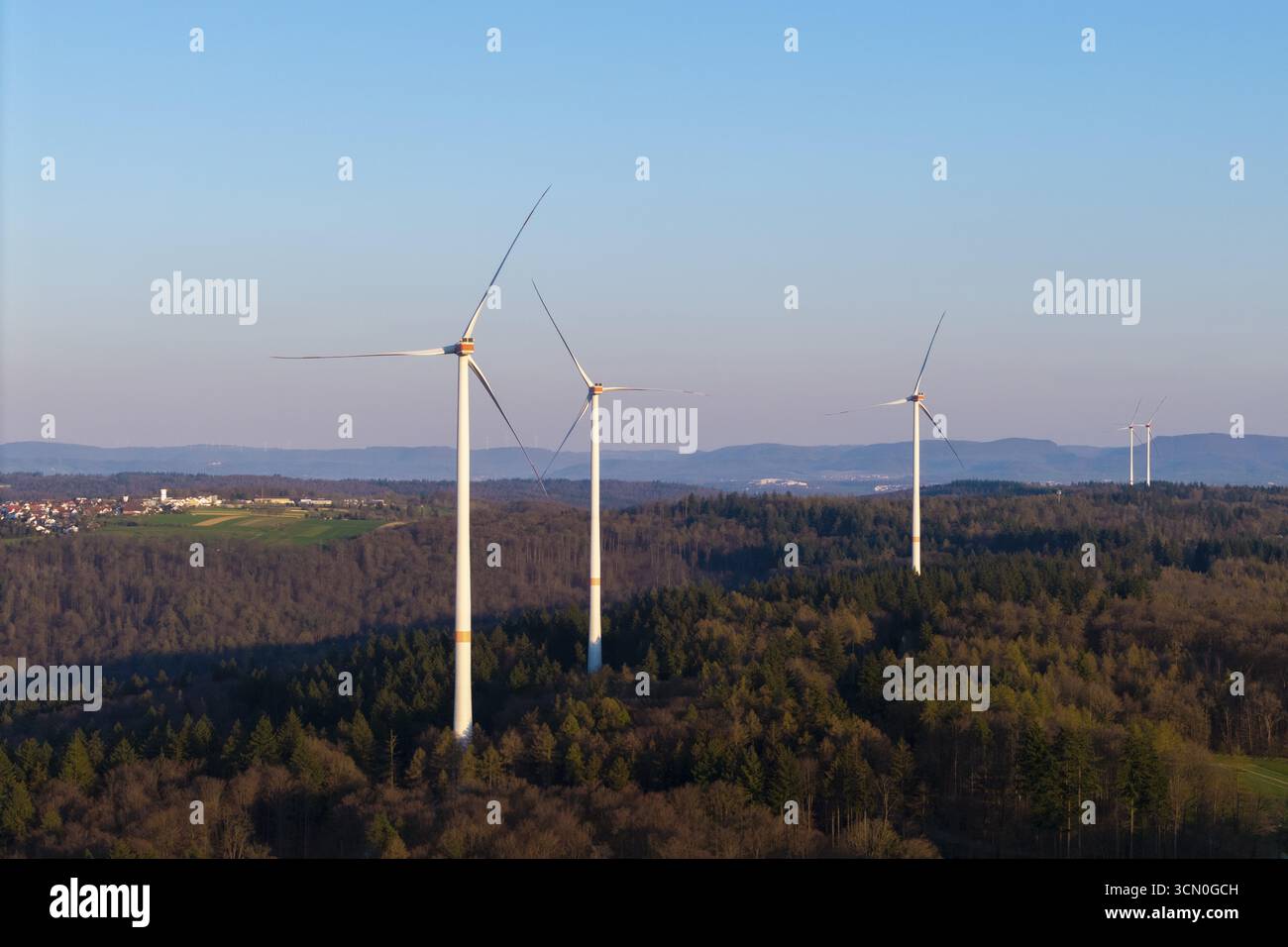 Diverse turbine eoliche si estendono attraverso un paesaggio boscoso sotto un cielo limpido, vicino a Schorndorf nella valle del Rems, Baden-Wuerttemberg, Germania Foto Stock