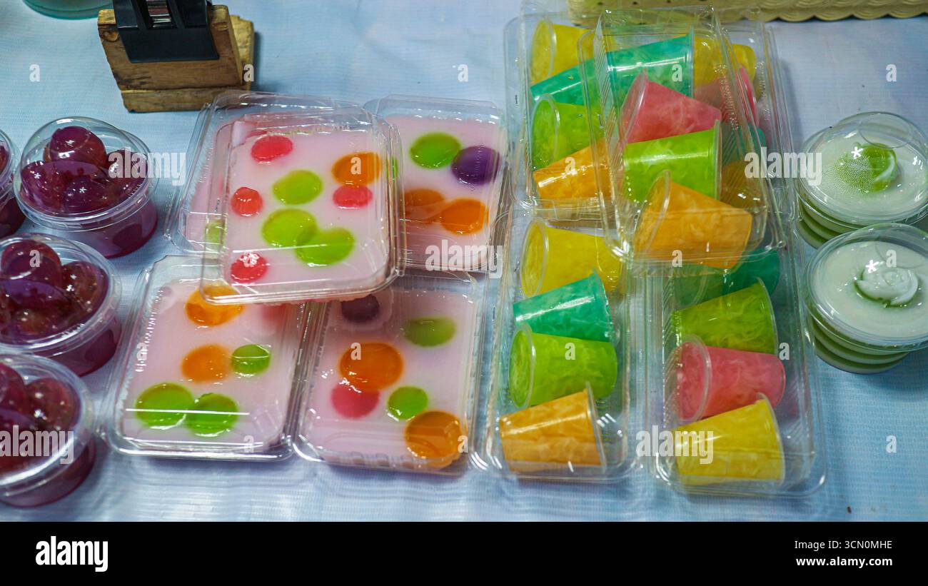 Dessert in gelatina tailandese assortito con latte di cocco, forme geometriche colorate e rotonde in vassoi di plastica, che riflettono le vivaci tradizioni dolci asiatiche. Foto Stock