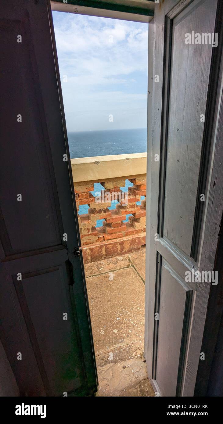 Splendida vista dell'oceano incorniciata da porte grigie. Una luminosa balaustra geometrica in mattoni rossi contrasta nettamente con il mare e il cielo azzurri. Foto Stock