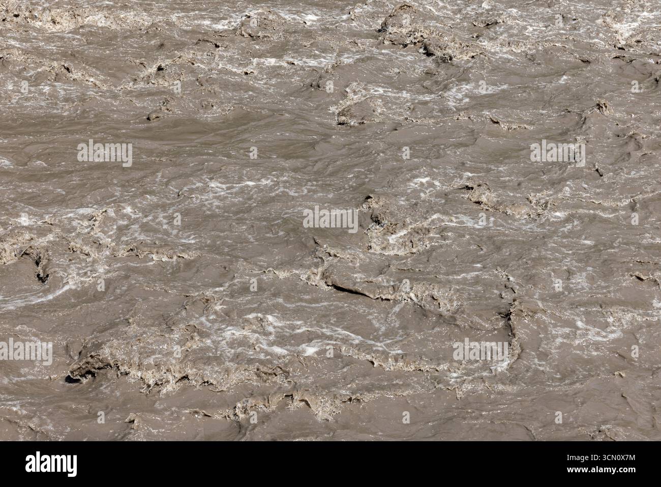 L'acqua bruna fluviale scorre intensamente, mostrando una corrente dinamica ed energica con turbolenza schiumosa e schemi turbolenti causati da movimenti rapidi Foto Stock