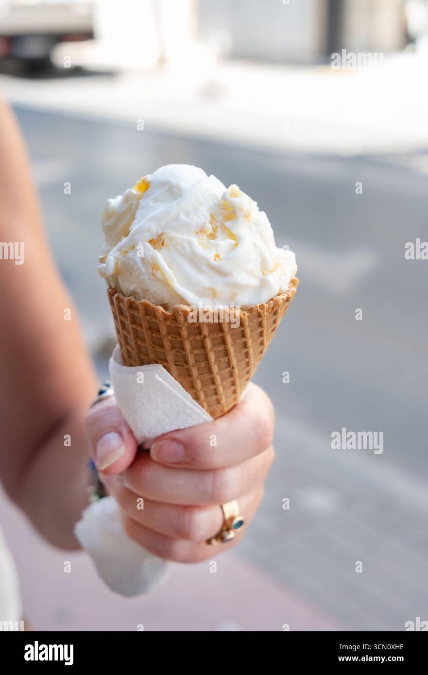 Rethymno, Creta, Grecia. Una donna che tiene una grande tazza di gelato in un cono di waffle. Il gelato ha un sapore di torta all'arancia Foto Stock