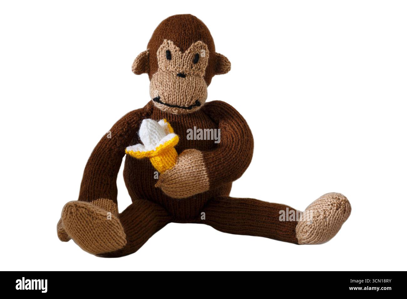 Scimmia lavorata a maglia seduta tenendo la banana isolata su sfondo bianco - animale a maglia Foto Stock