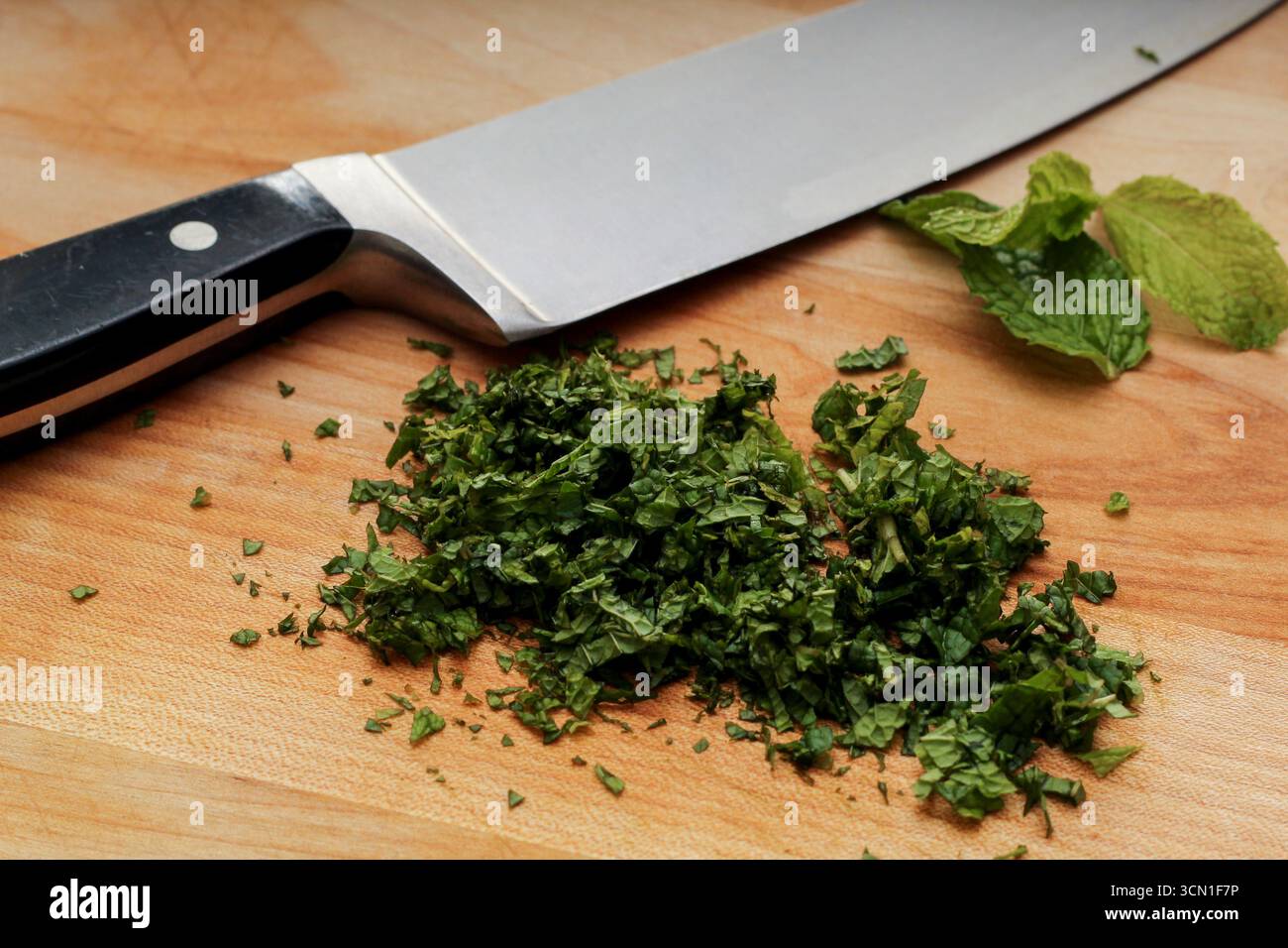Foglie di menta tritate e coltello da cucina su tagliere in legno Foto Stock