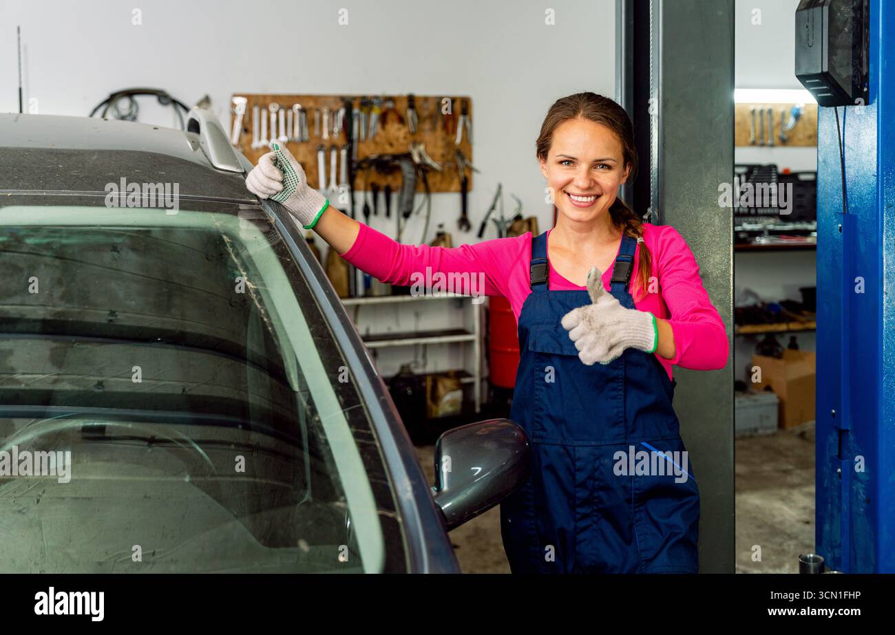 Meccanico donna che dà il pollice in officina di riparazione auto, donna professionista nell'assistenza automobilistica Foto Stock