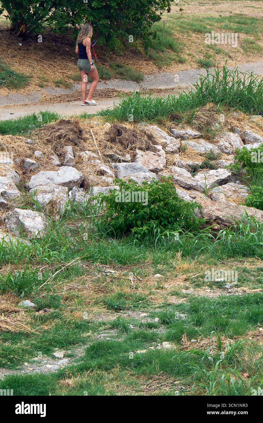 Viladecans. Barcellona - 18 settembre 2025: Una donna viene catturata camminando su un sentiero vicino a un pendio roccioso e erboso, che ritrae un momento informale di Foto Stock Viladecans. Barcellona - 18 settembre 2025: Una donna viene catturata camminando su un sentiero vicino a un pendio roccioso e erboso, che ritrae un momento informale di Foto Stock
