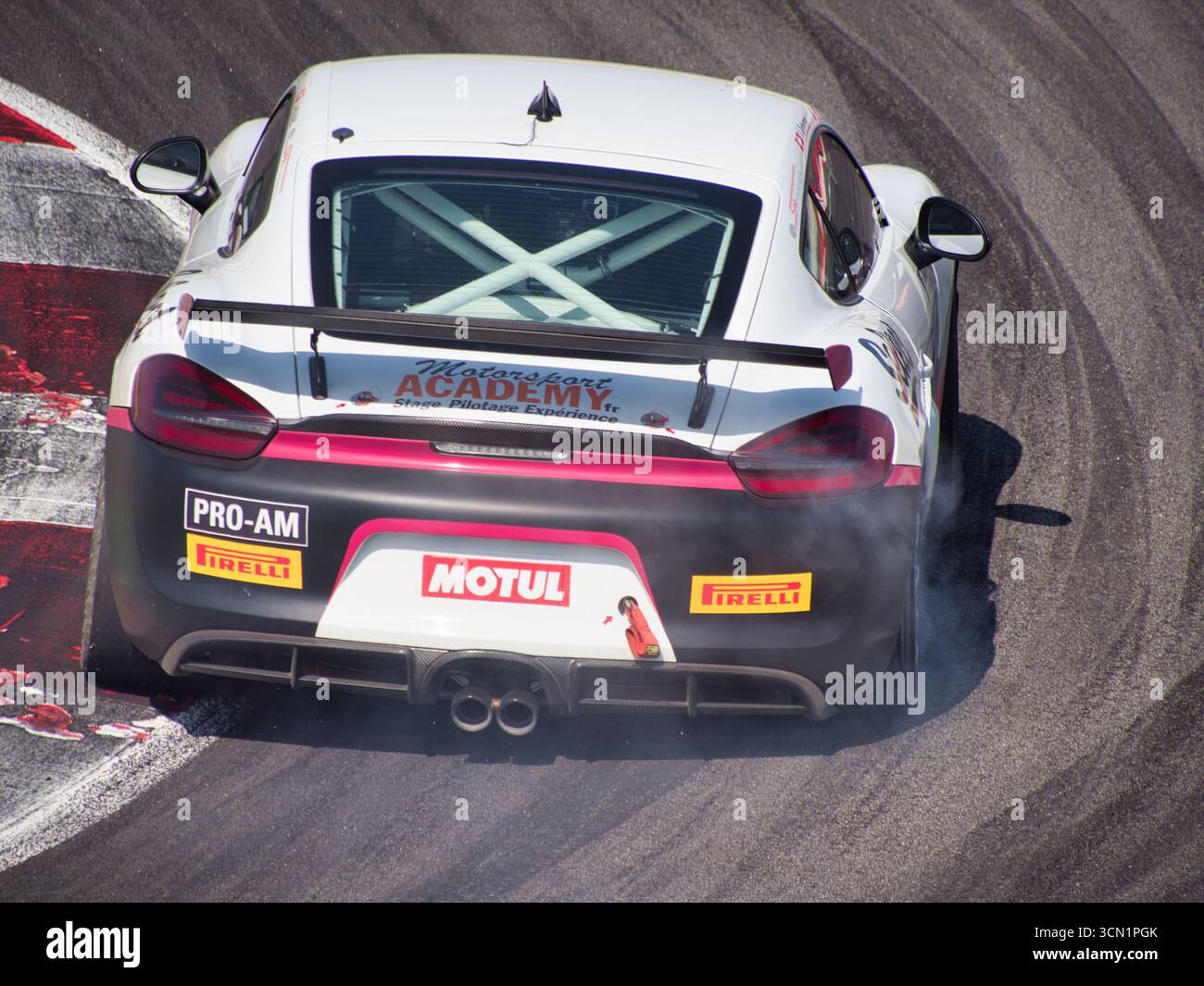 Auto da corsa scivolando in curva con Tire Smoke - Un'auto sportiva ad alte prestazioni corre dietro una curva stretta, con una leggera deriva e fumo proveniente dalla sua Foto Stock
