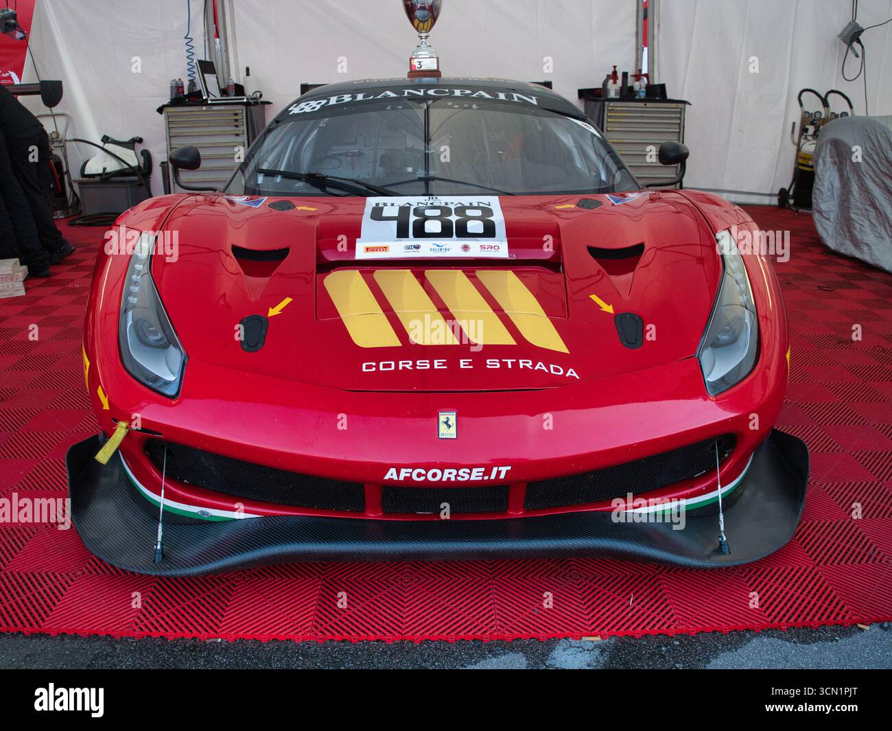 Vista frontale di una Ferrari 488 da corsa rossa - Una vista frontale simmetrica di una Ferrari 488 GT rossa con un trofeo sul tetto, parcheggiata all'interno di un professionista Foto Stock