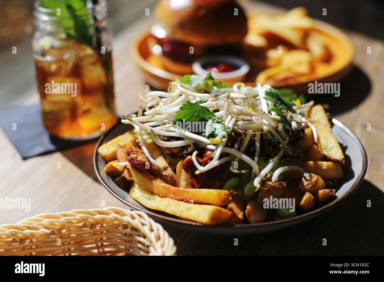Ciotola di patatine fritte con condimenti. Cibo di strada servito con hamburger. Primo piano sul concetto di fast food. Delizioso spuntino con verdure. Foto Stock