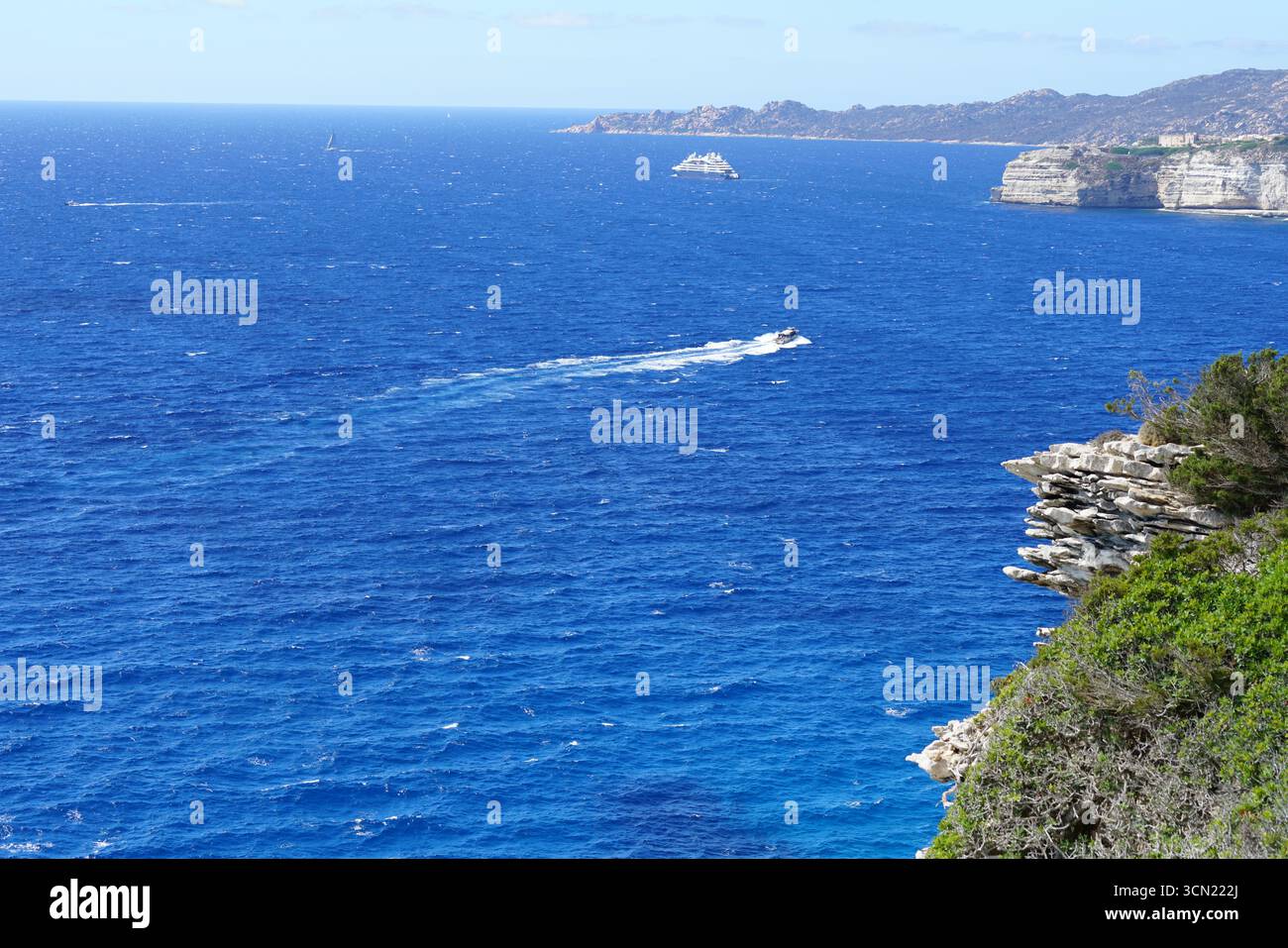 Vivace vista sull'oceano lungo la costa frastagliata con Blue Water, Boat Wake e scogliere. Bonifacio, Corsica, Francia Foto Stock
