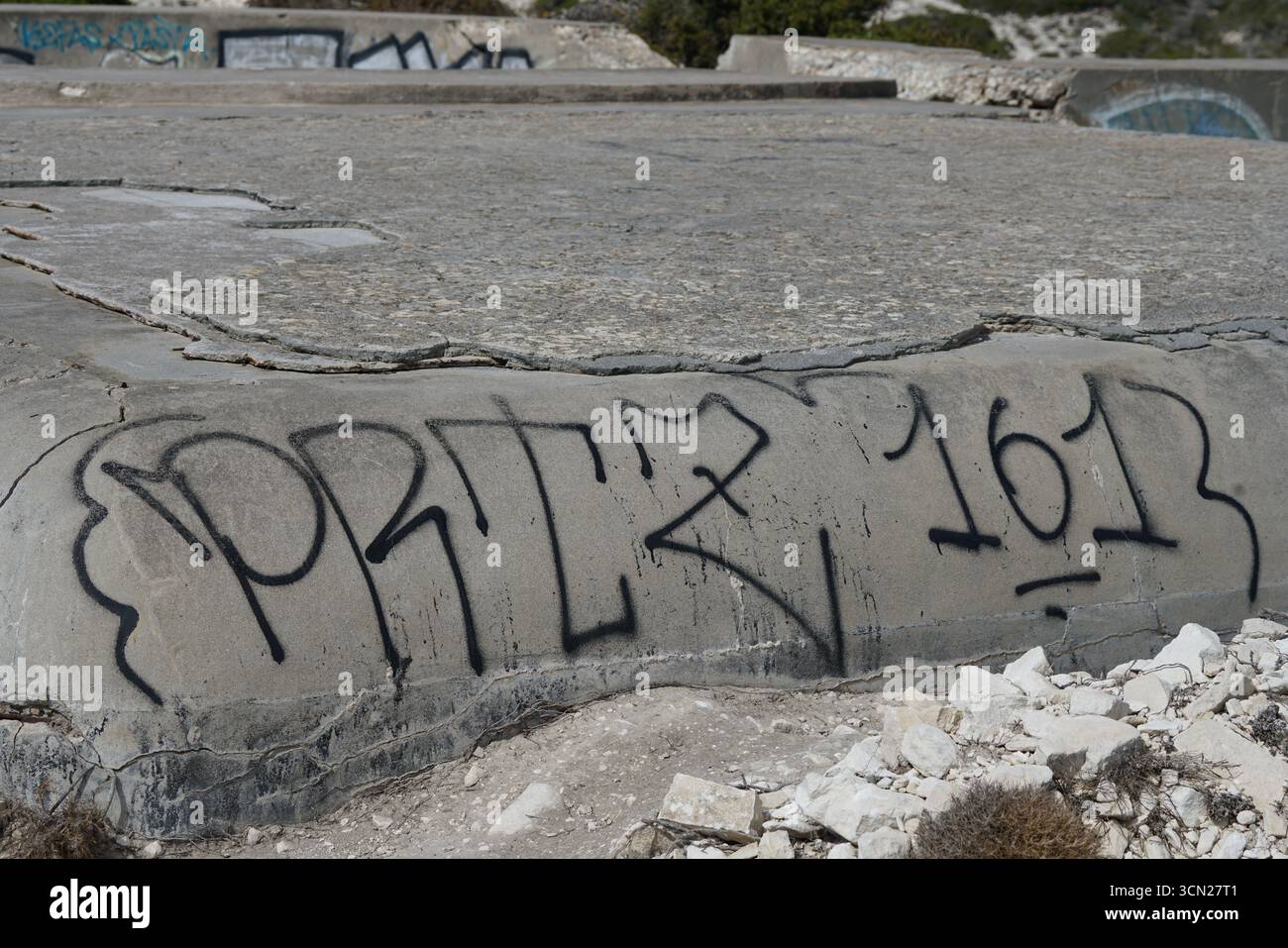 Graffiti sul muro di cemento incrinato nel sito abbandonato con rocce e degrado urbano. Bonifacio, Corsica, Francia Foto Stock