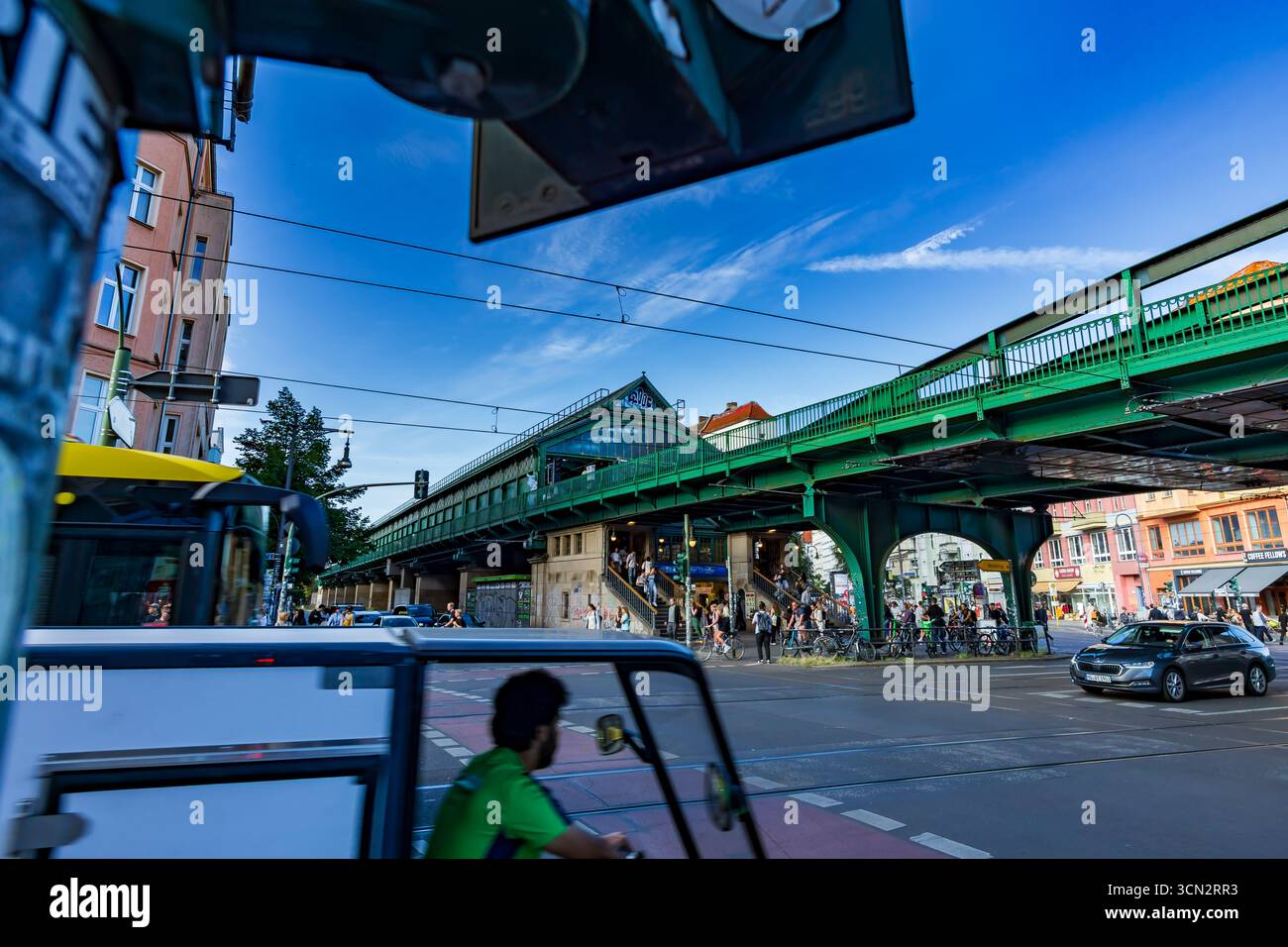 Vista urbana più ampia della U-Bahn Eberswalder Straße con ciclista sfocato, semafori e vita di strada dinamica di fronte alla stazione. Foto Stock