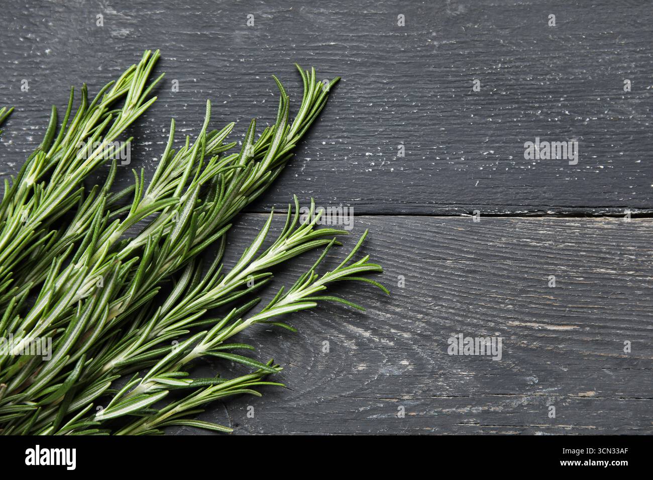 Ramoscelli di rosmarino freschi su sfondo di legno nero Foto Stock