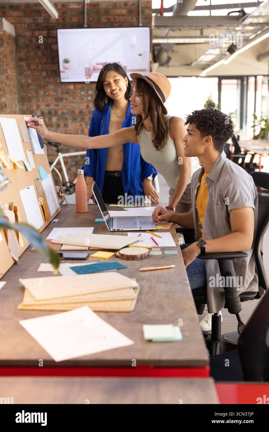 Diversi colleghi che collaborano al tavolo in ufficio con laptop, tavola in sughero e appunti Foto Stock