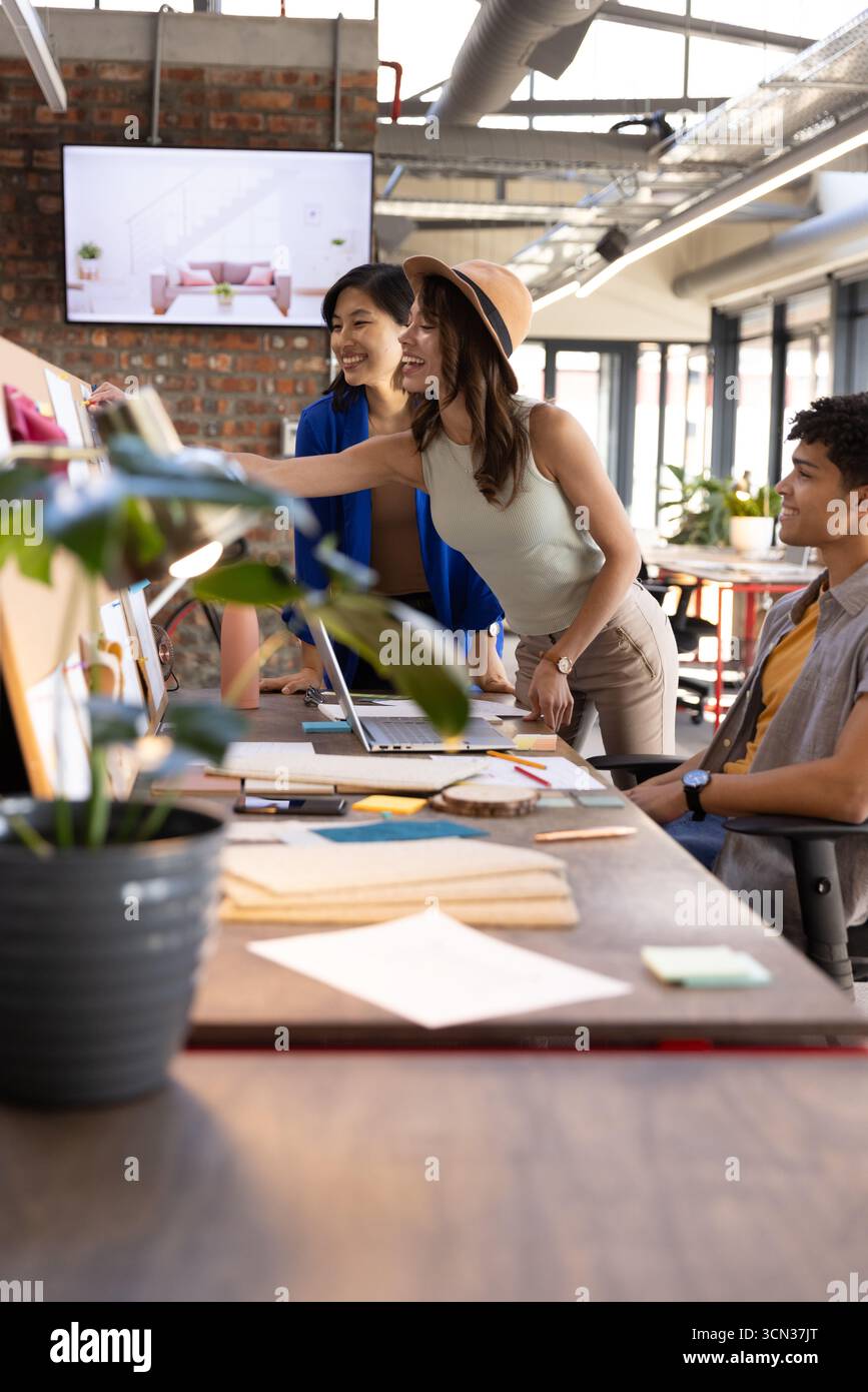 Colleghi diversi che discutono di design alla scrivania con laptop, campioni di tessuto e appunti adesivi Foto Stock