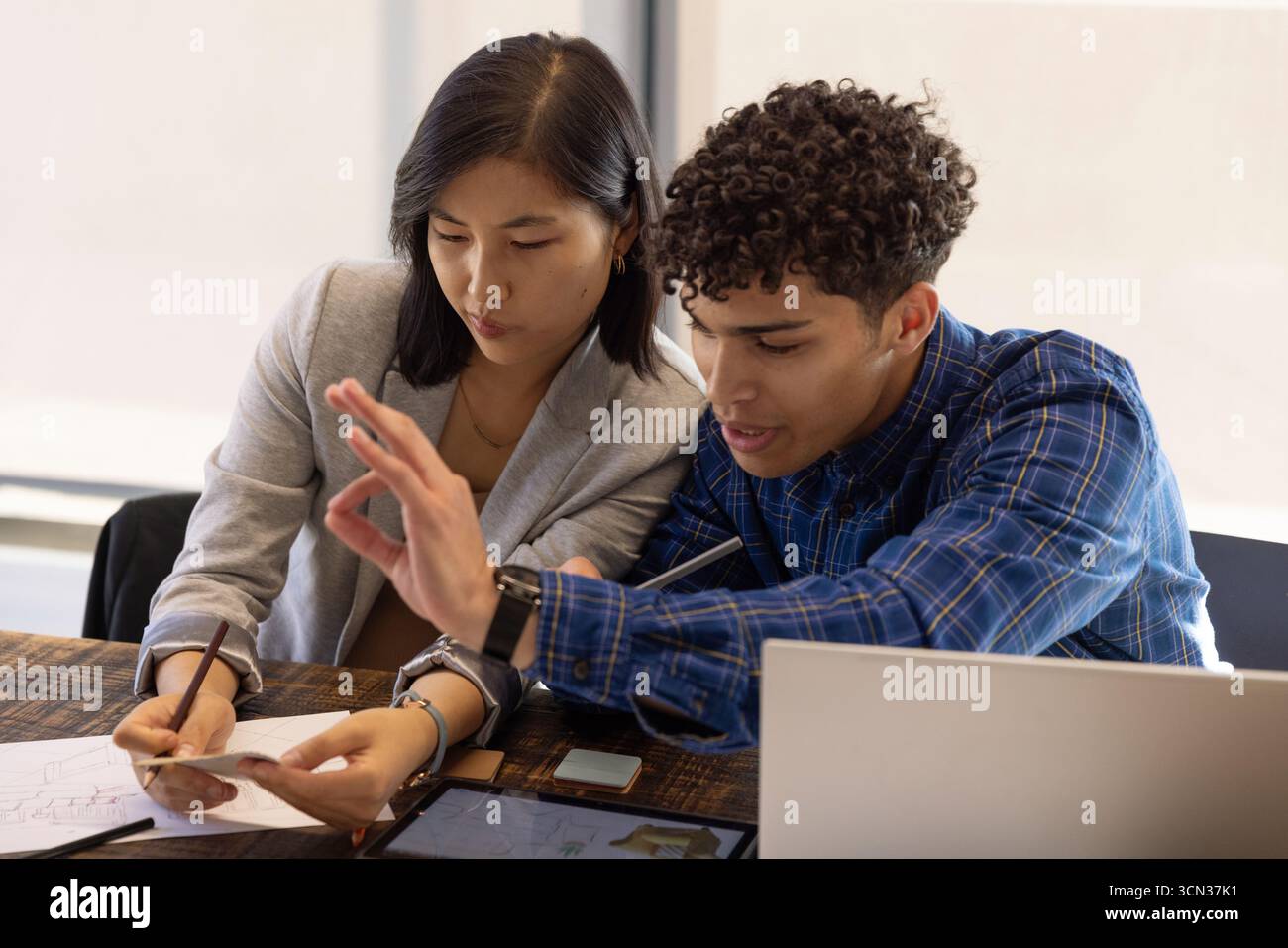 Diversi colleghi che collaborano al tavolo di legno in ufficio utilizzando computer portatile, tablet e schizzi stampati Foto Stock