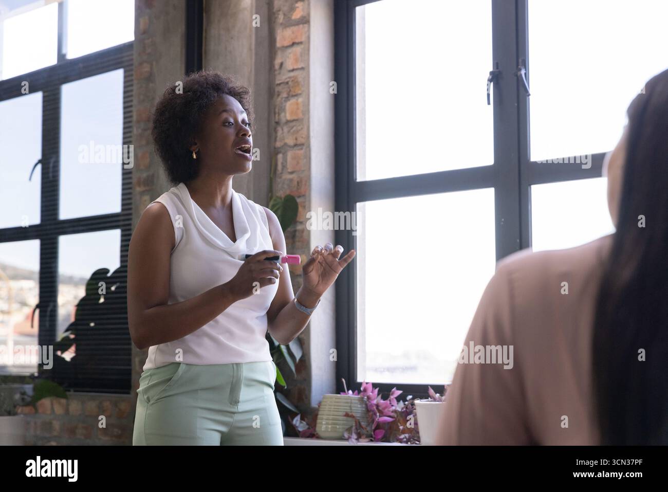 Diversi colleghi che presentano idee al tavolo dell'ufficio con pennarello, vaso di fiori, tazza da caffè Foto Stock
