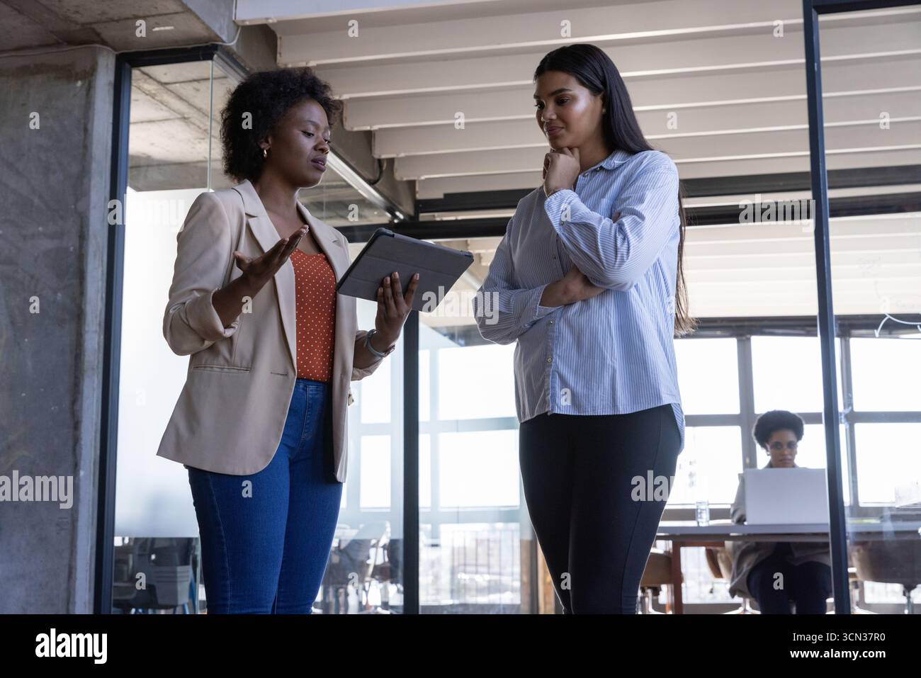 Colleghi diversi che discutono i dettagli del progetto in ufficio vicino alla partizione in vetro con tablet e laptop Foto Stock