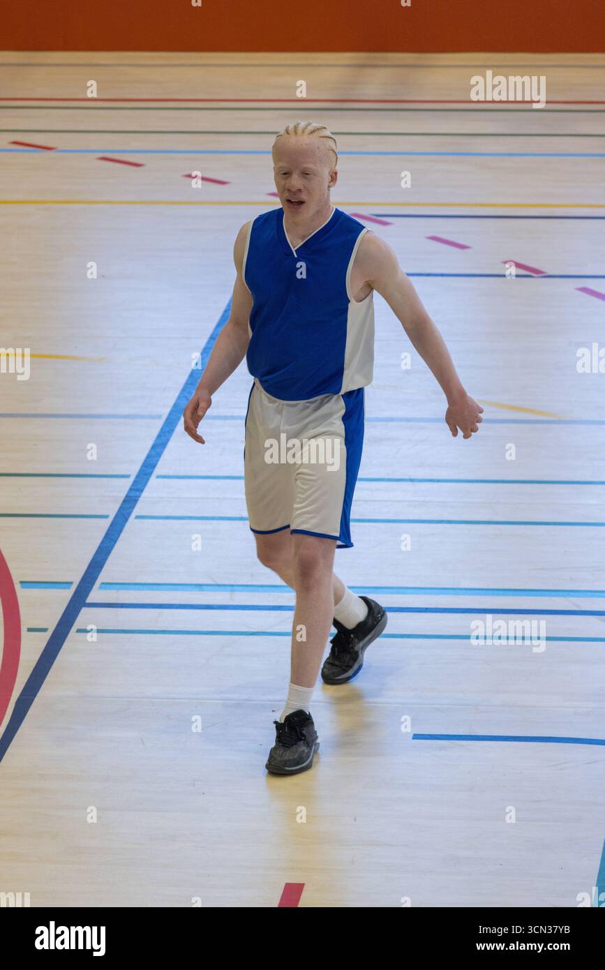 Atleta maschile con albinismo che cammina sul campo da palestra con linee che indossano Jersey e sneaker Foto Stock