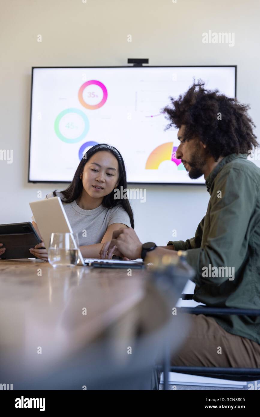 Colleghi diversi che collaborano a progetti aziendali in sala conferenze utilizzando tablet e monitor Foto Stock
