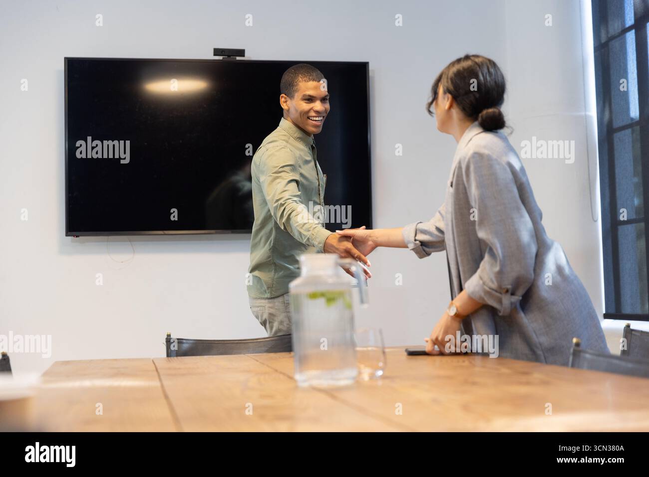 Diversi colleghi che stringono la mano sul tavolo da conferenza nella sala riunioni con pitche e smartphone Foto Stock