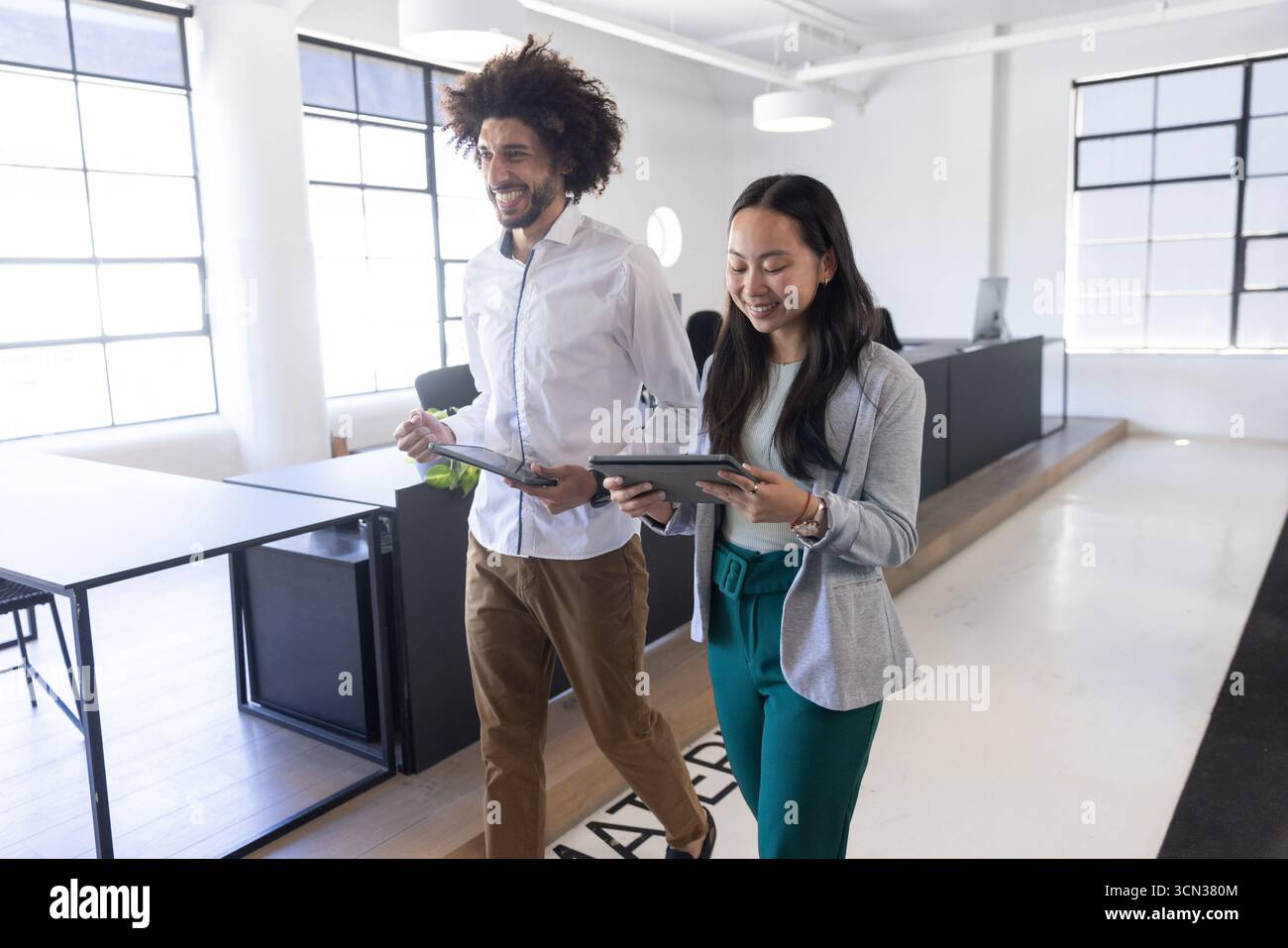 Colleghi diversi che camminano in un moderno ufficio open space con tablet, discutendo del progetto Foto Stock