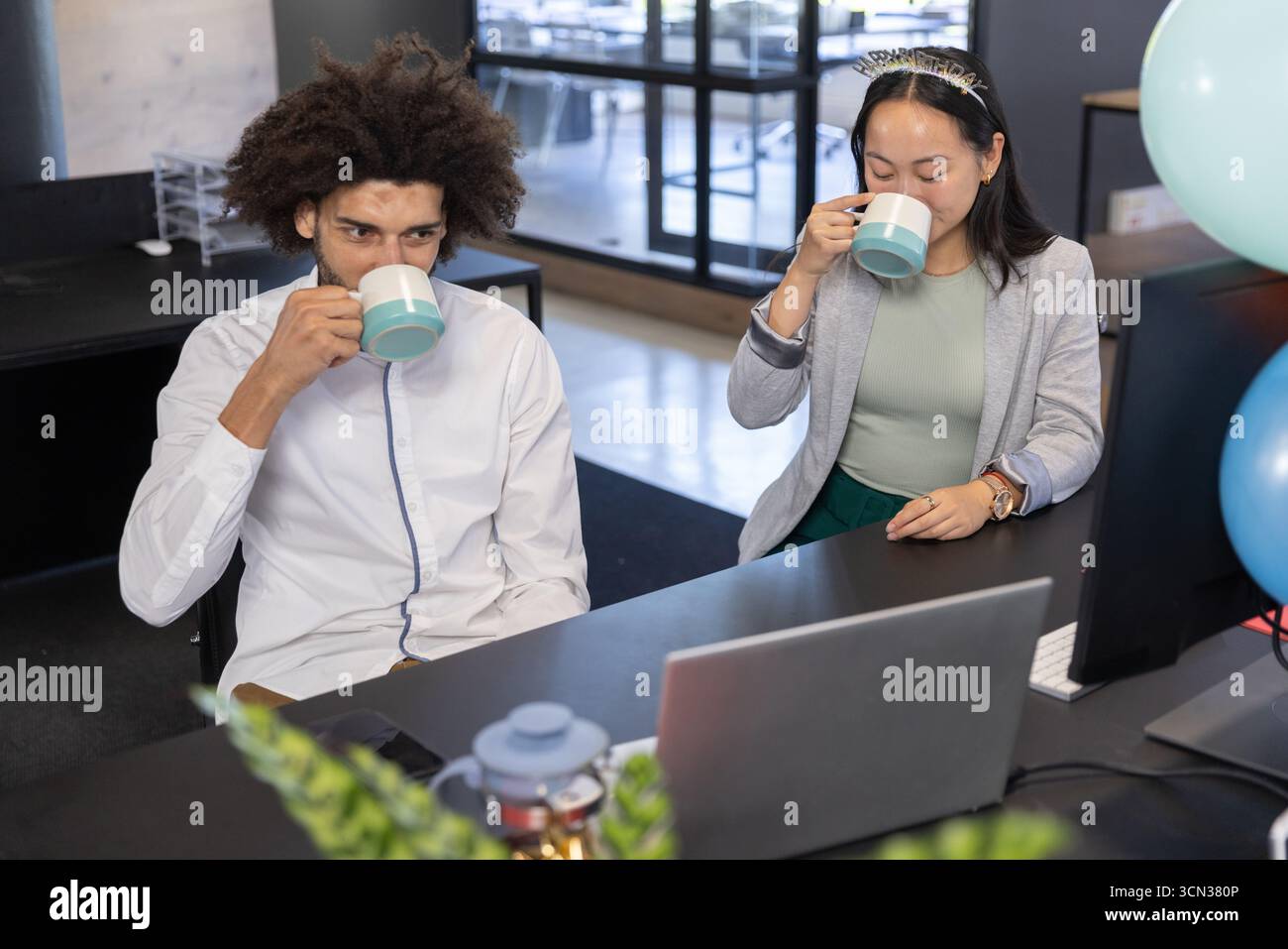 Diversi colleghi che sorseggiano caffè da tazze di tè abbinate alla scrivania con teiera in ufficio Foto Stock