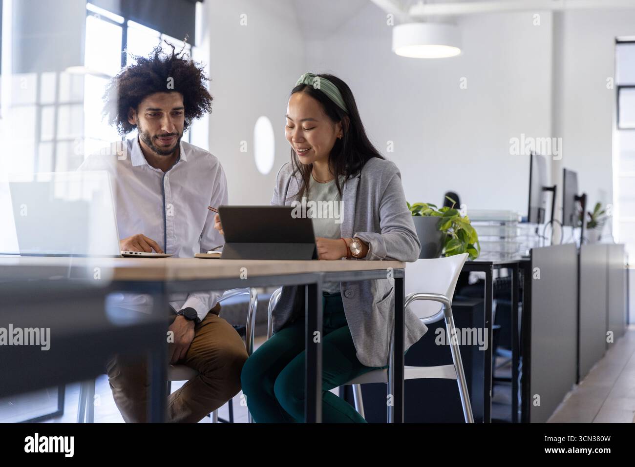 Colleghi diversi che collaborano su tablet e notebook a un tavolo alto in ufficio Foto Stock