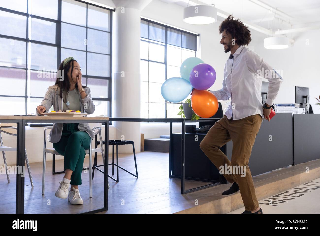 Diversi colleghi che celebrano la sorpresa del compleanno in un abbigliamento da lavoro in ufficio con regali e palloncini Foto Stock