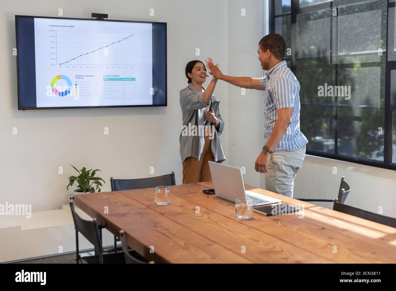Diversi colleghi che lavorano accanto a un tavolo in legno con computer portatile e che espongono le tabelle sullo schermo dell'ufficio Foto Stock