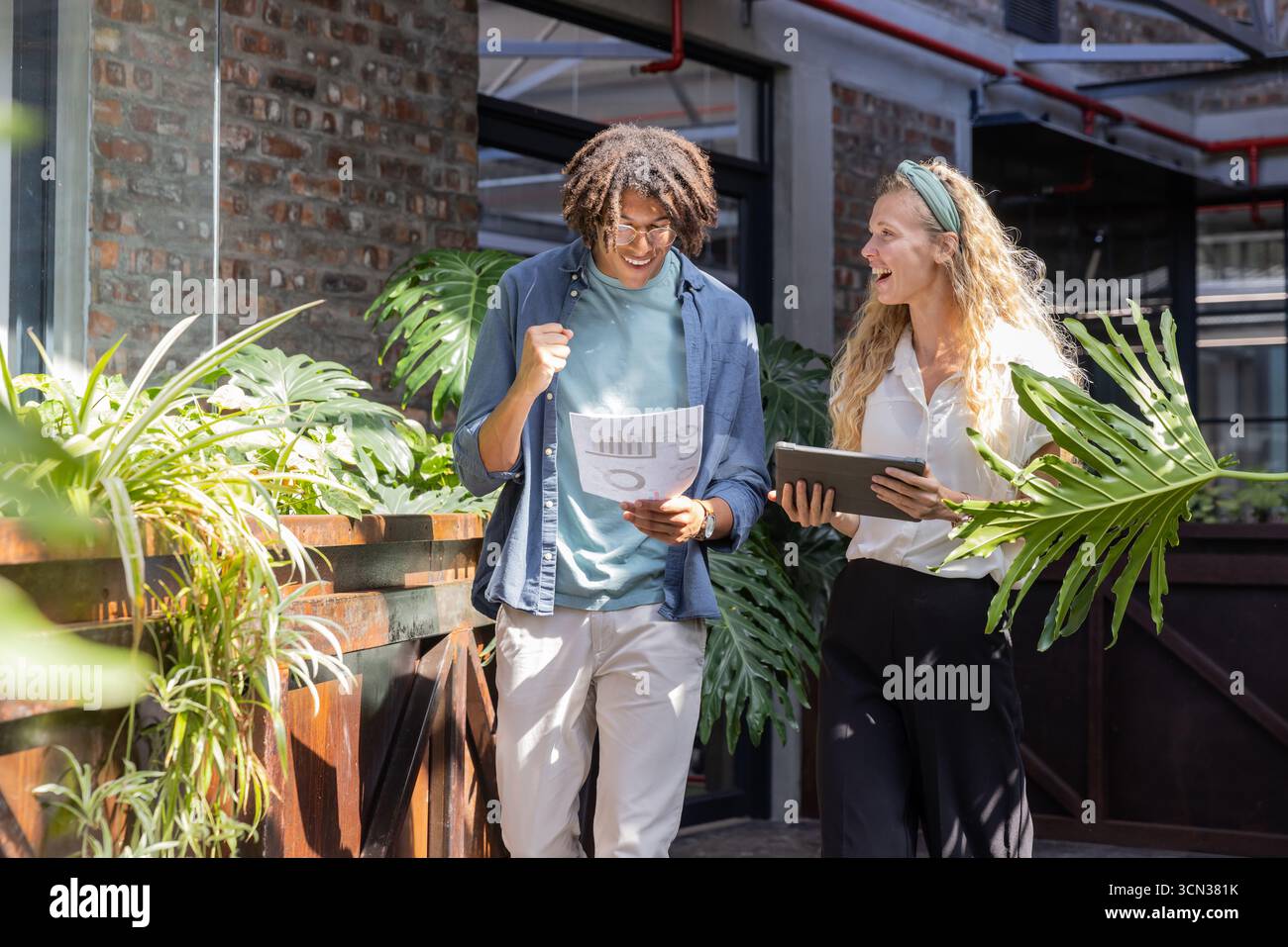 Diversi colleghi che camminano nei corridoi dell'ufficio che esaminano il referto stampato e il tablet con gli occhiali delle piante Foto Stock