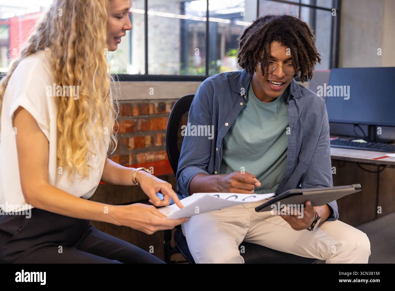 Colleghi diversi seduti che esaminano documenti stampati, tablet e monitor presso la moderna scrivania dell'ufficio Foto Stock