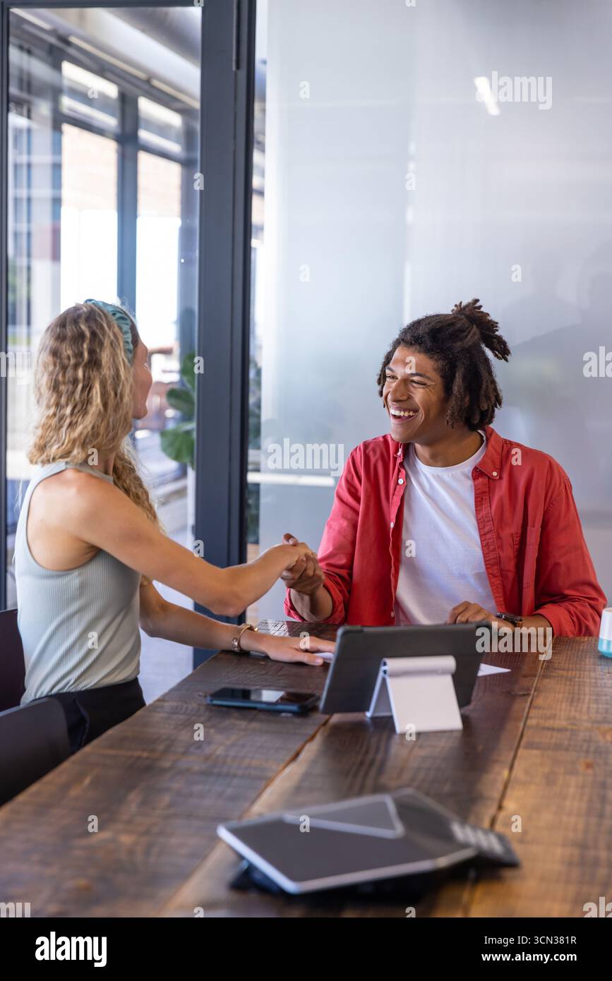 Diversi colleghi stringono la mano sul tavolo da conferenza in ufficio con un tablet e una tazza da caffè Foto Stock