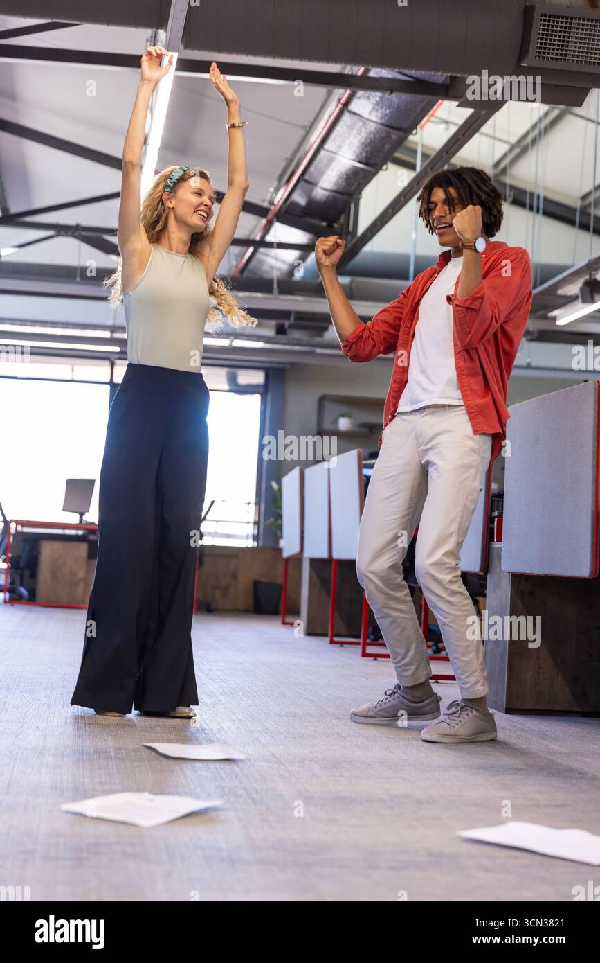 Diversi colleghi che celebrano il recente successo vicino a documenti sparsi sul pavimento in un ufficio open space Foto Stock
