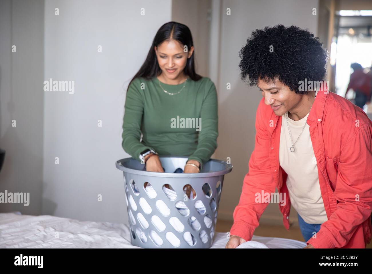 Diverse coppie di capi lavati e pieghevoli nella camera da letto di casa con cestino per la lavanderia Foto Stock