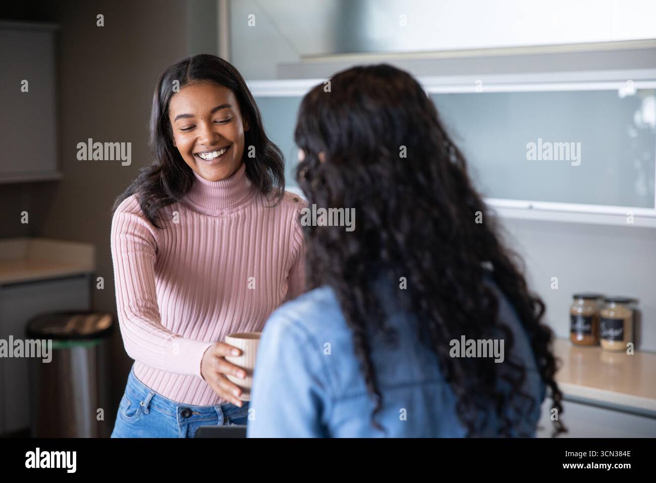 Diverse collaboratrici si scambiano la tazza del caffè nell'angolo cottura dell'ufficio con vasetti e cestino Foto Stock