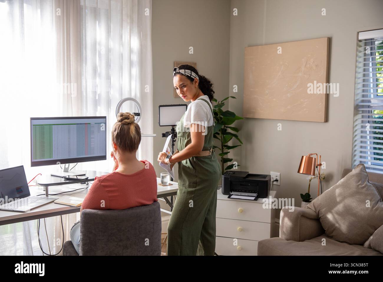 Diverse collaboratrici che collaborano alla stesura di un foglio di calcolo in un ufficio domestico con luce anulare e fotocamera Foto Stock