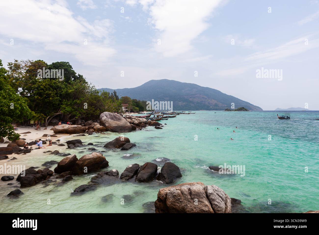 Koh Lipe, Thailandia. Acqua verde smeraldo cristallina, sabbia, rocce, barche, alberi, montagna e cielo. Foto Stock