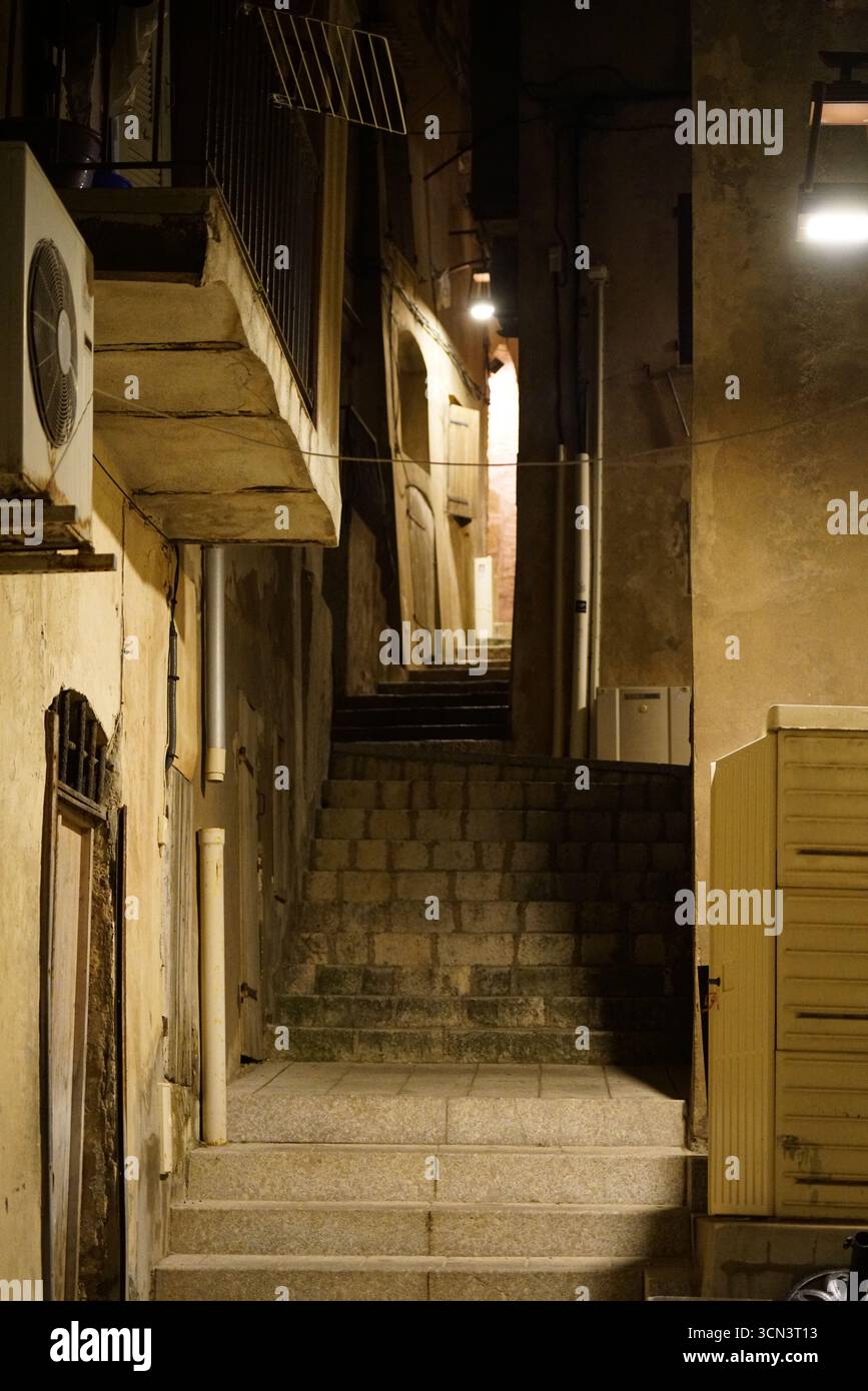 Scala notturna dei vicoli urbani poco illuminata con passaggi stretti e vecchi edifici. Bonifacio, Corsica, Francia Foto Stock