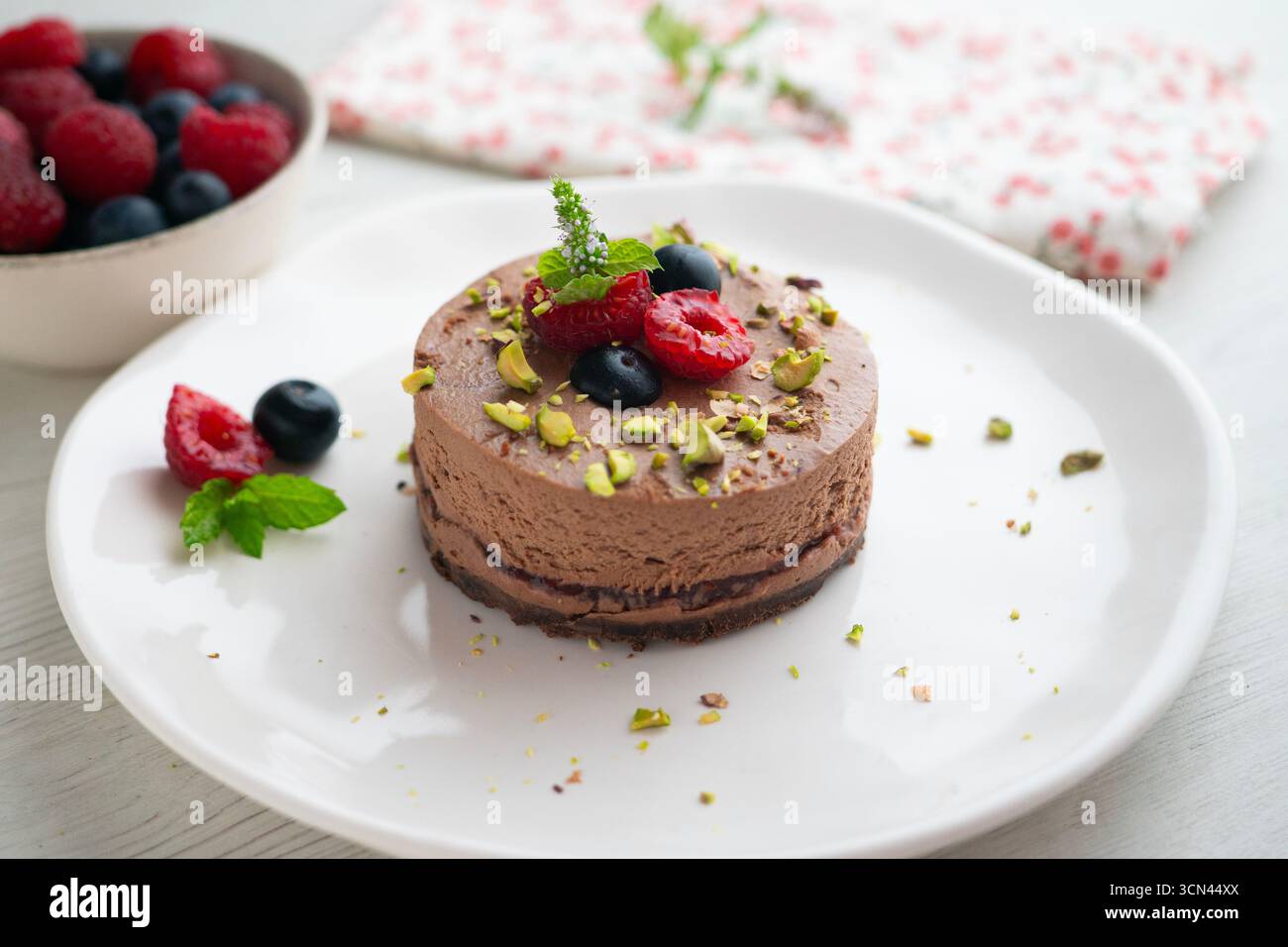 Crostata con mousse al cioccolato ripiena di marmellata e decorata con pistacchi e frutti di bosco rossi. Foto Stock
